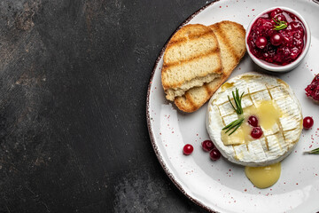 Baked camembert cheese with cranberries, basil leaves and rosemary on dark table. French cuisine. place for text, top view - obrazy, fototapety, plakaty