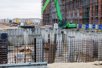 A construction excavator and a multi-storey fortified building under construction against a gray sky background.