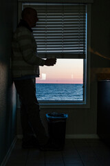 Norfolk, Virginia, USA A man drinks coffee alone in a motel room by the sea.