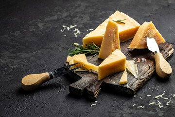 Parmesan cheese on a wooden board, Hard cheese, rosemary and cheese knife on a dark background....