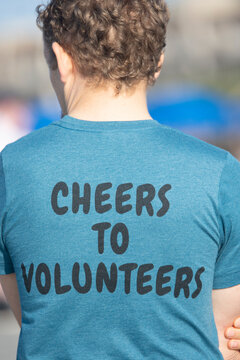 The back of a male with curly hair wearing a volunteer t-shirt.