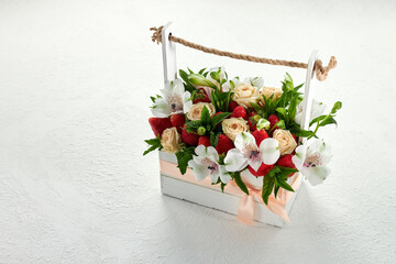 Wooden box filled with ripe strawberries and beautiful white and pink flowers on a white background