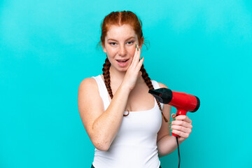 Young caucasian reddish holding a hairdryer isolated on blue background whispering something