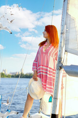 Attractive girl looking into the distance in a pink mini dress on a yacht. Background - seagulls in the sky, clouds. Sea walk, travel, sea. Concept summer, rest.