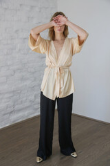 Studio serie of imges of young woman in beige silk robe and black wide trousers