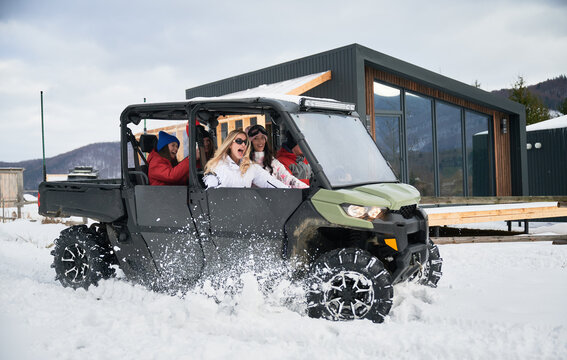 Happy women riding on off-road buggy car. Contemporary barnhouse on background. Concept of active leisure and winter activities.
