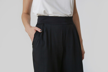 Female model wearing white camisole cotton top and black trousers. Classic and simple summer fashion. Studio shot.