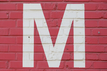 White letter M painted to brick wall on red background (from a letter set containing B, C, D, F, G,...