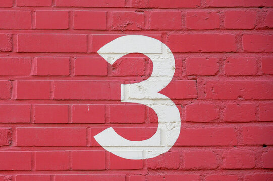 White number 3 painted to brick wall on red background (from a letter set containing B, C, D, F, G, M, R and 1, 3, 4)