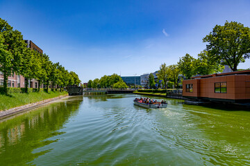 Fototapeta na wymiar A tourist boat full of people sailing down the water canal with rows of green trees on a summer sunny day