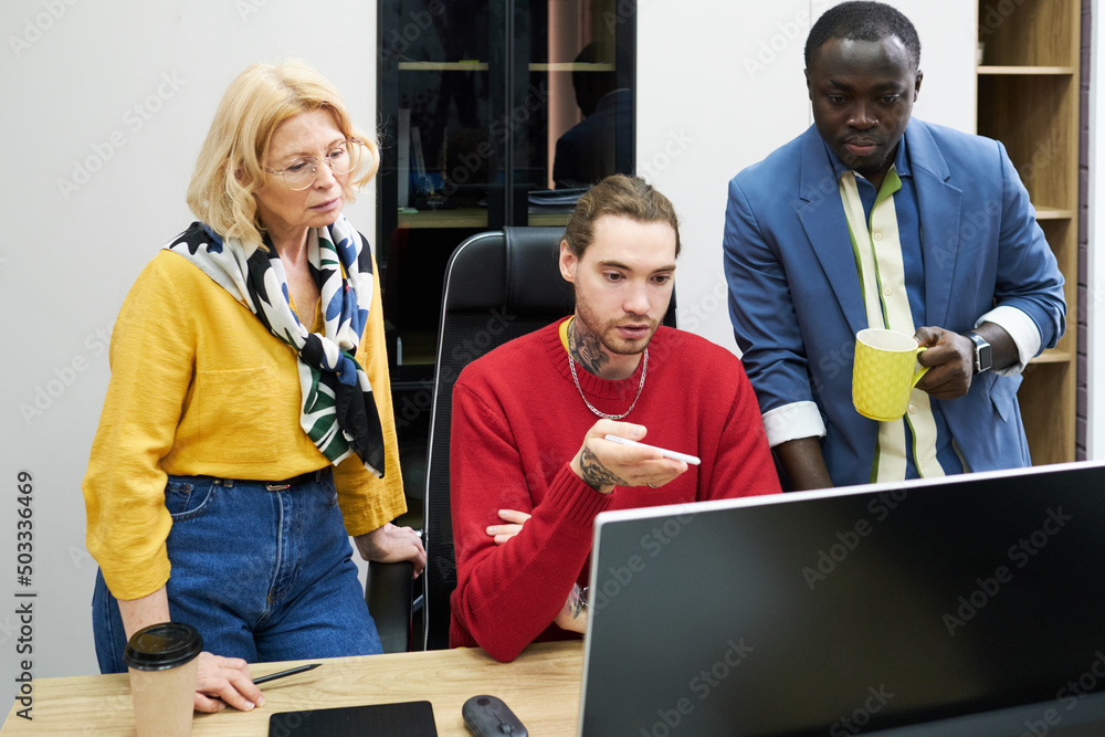 Poster Group of graphic designers looking at computer monitor and discussing project in team at office