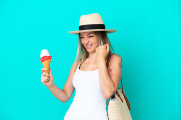 Young Romanian woman holding ice cream and beach bag isolated on blue background celebrating a victory