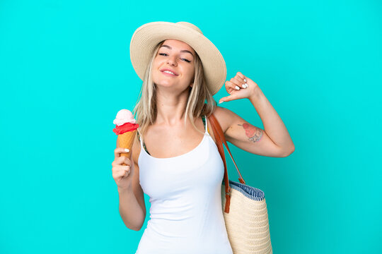Young Romanian woman holding ice cream and beach bag isolated on blue background proud and self-satisfied