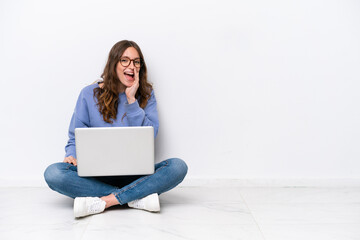 Young caucasian woman with a laptop sitting on the floor isolated on white background shouting with mouth wide open