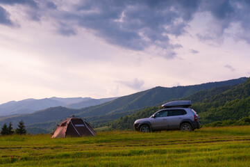 Fototapeta na wymiar A brown tent and an old car with a trunk on the roof. Quick installation system. Summer day. Mountains and forest, travel and tourism concept. Camping.