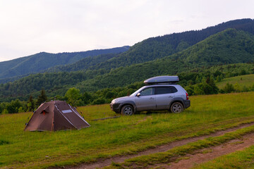 A brown tent and an old car with a trunk on the roof. Quick installation system. Summer day. Mountains and forest, travel and tourism concept. Camping.