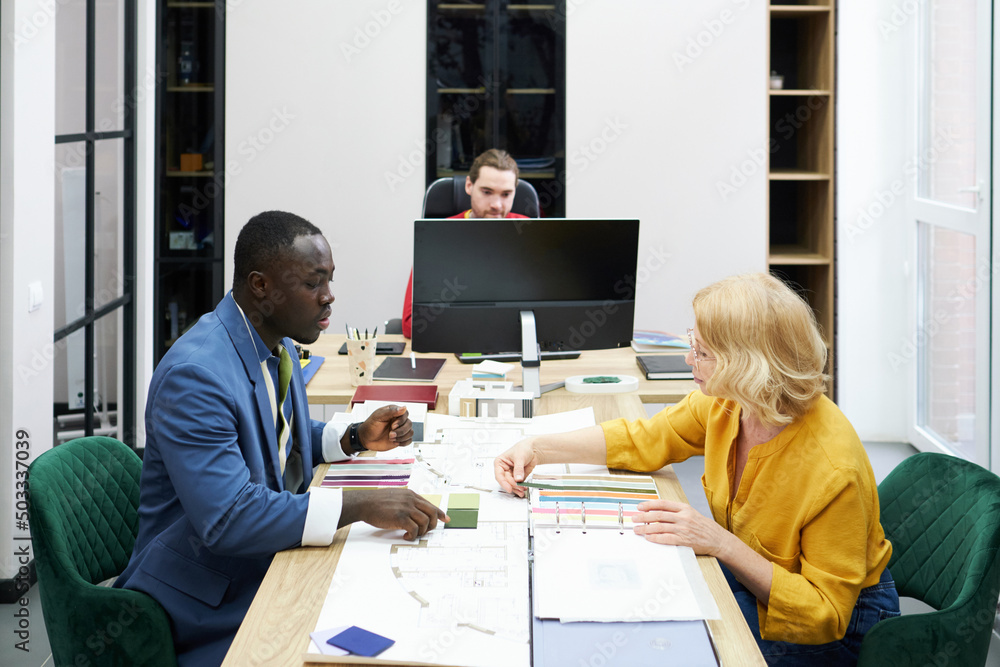 Poster Professional designers using palette to choose colour for new apartment project while sitting at table at meeting