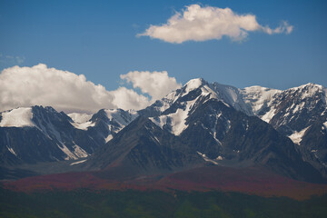 Landscape with snow-capped mountains and blue cloudy sky.