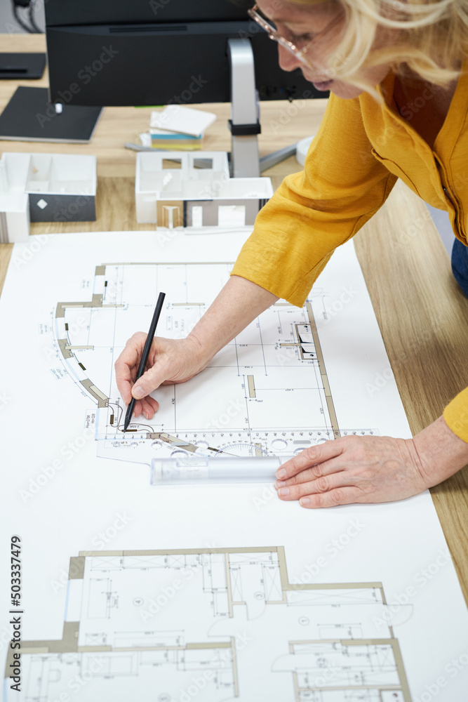 Poster close-up of mature female architect drawing project with pencil and ruler at table
