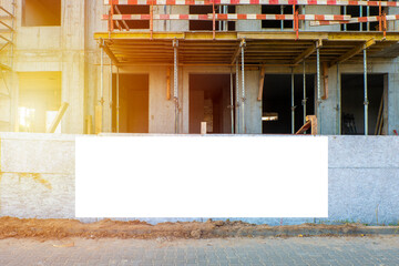 Blank white advertising billboard on the fence of construction site. Sunny summer evening.