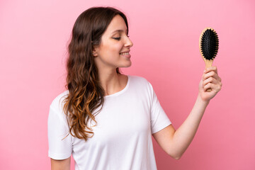 Young caucasian woman with hair comb isolated on pink background with happy expression