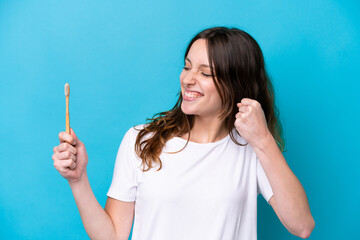 Young caucasian woman brushing teeth isolated on blue background celebrating a victory