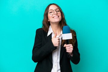 Fototapeta premium Young TV presenter woman isolated on blue background giving a thumbs up gesture