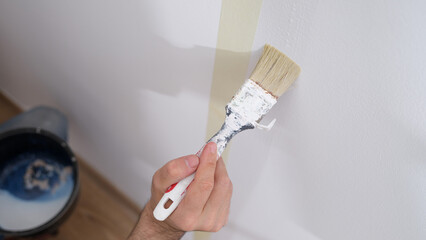 Manual worker holding brush and painting with white on wall of house