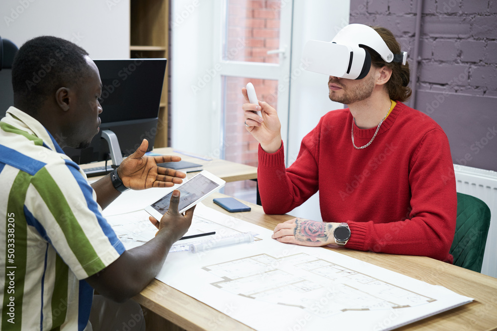 Poster Business people sitting at table with blueprint using digital tablet to connect with VR goggles during teamwork at office