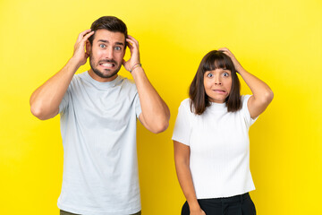 Young couple isolated on yellow background takes hands on head because has migraine
