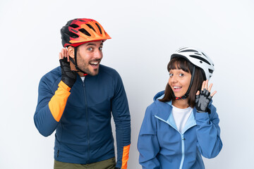 Young cyclist couple isolated on white background listening to something by putting hand on the ear