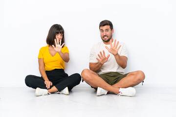 Fototapeta na wymiar Young couple sitting on the floor isolated on white background is a little bit nervous and scared stretching hands to the front