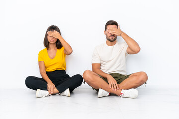 Young couple sitting on the floor isolated on white background covering eyes by hands. Do not want to see something