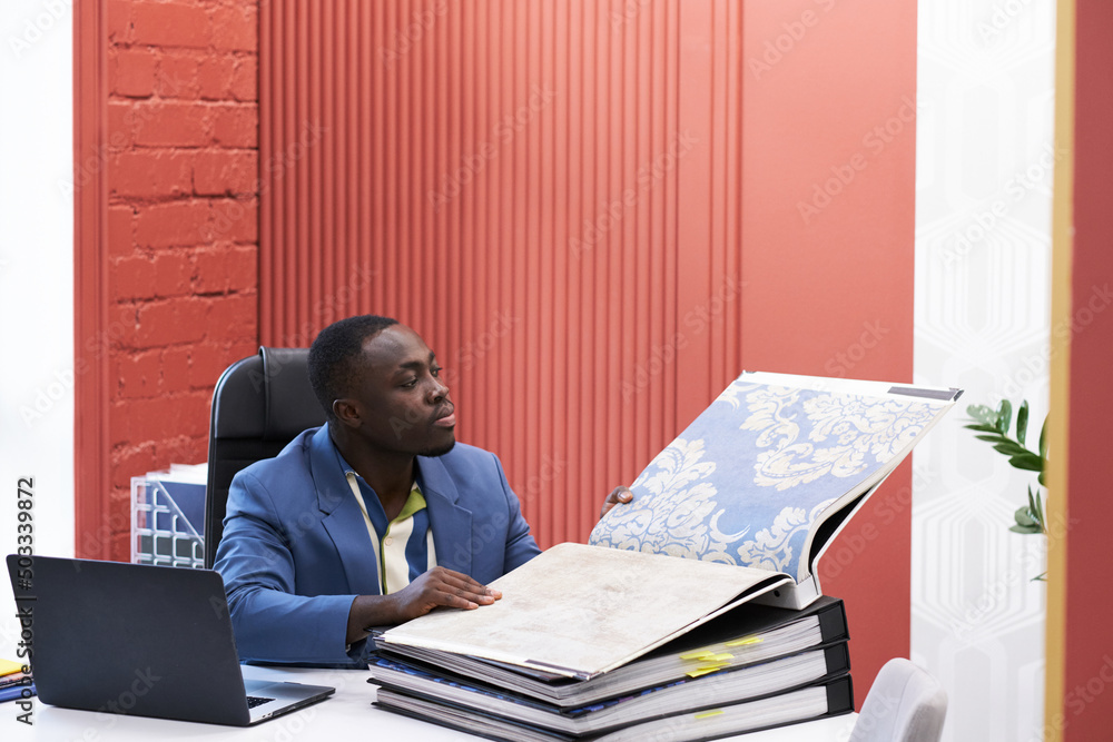 Aufkleber african young designer examining sample of fabric in folder for future interior while sitting at tab