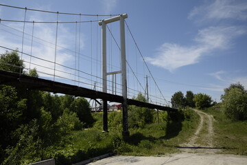 Metal suspension bridge over the river through dense vegetation. Ulyanovsk Russia.