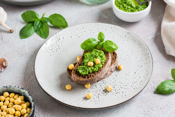 Appetizing bruschetta made from rye bread, pesto and chickpeas on a plate on the table.