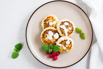 Cottage cheese pancakes with sour cream, raspberries and mint on a plate. Top view. Close-up