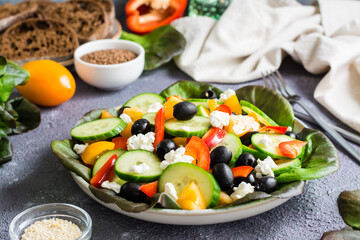 Greek salad of tomatoes, cucumbers, peppers, olives, lettuce and cheese on a plate on the table.