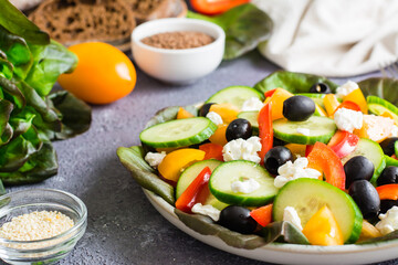 Greek salad of tomatoes, cucumbers, peppers, olives, lettuce and cheese on a plate.  Close-up