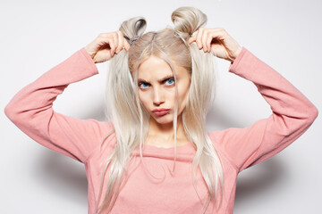 Pretty blonde girl holding she's hair buns in pink shirt, on white background.