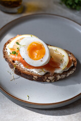 Healthy breakfast or snack with medium boiled eggs on toasted bread with cheese cream, salmon and lemon slices on grey plate