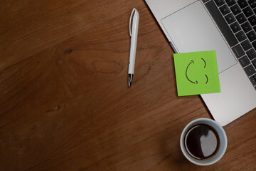 Concept du bonheur et du bien-être au travail. Une note sur un papier est collée sur un ordinateur portable avec le dessin d'un sourire. Un café est posé sur la table.
