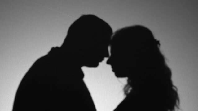Silhouette of couple in love on white background. Shadow from people. Romantic feelings. Game of shadows. A male and female tenderly embrace. Soft focus. Black and white. Professional lighting