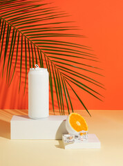 White colored can with cut in half orange fruit, ice and tropical palm leaf on product podium. Summer drink minimal concept.