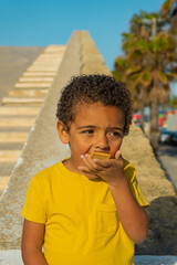 Fototapeta premium Black boy eating a cookie with chocolate. Dressed in yellow t-shirt, African American boy