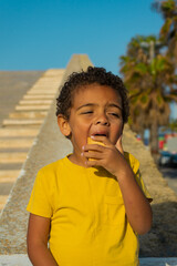 Fototapeta premium Black boy eating a cookie with chocolate. Dressed in yellow t-shirt, African American boy