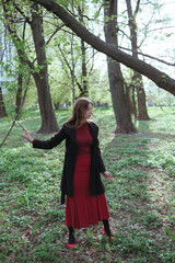 a girl with blonde hair in red golf and a skirt walks through the spring forest