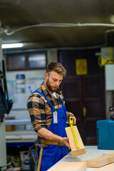 Portrait of young handsome caucasian carpenter who measures a board at the workshop