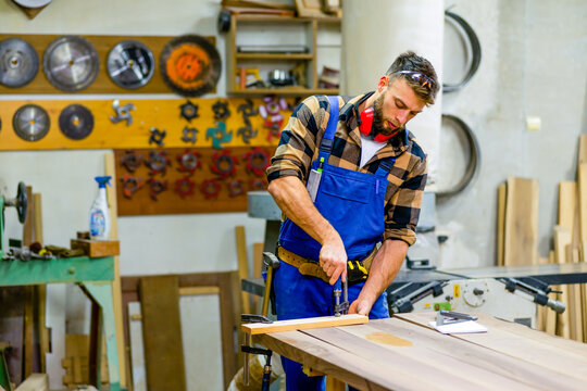 Young handsome caucasian carpenter working with clamps in workshop