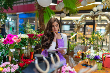 A beautiful worried and tired florist is sitting at the counter thinking about work, looking at her notebook